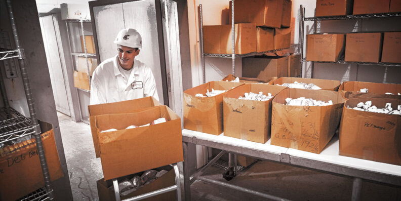 Man in white coat carries a box of prepared meat