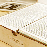 A close-up image of an open archival box containing neatly stacked, typewritten documents labeled "Daily annual 1960-1961." The documents are densely filled with text, and a black-and-white photograph is partially visible in the background.