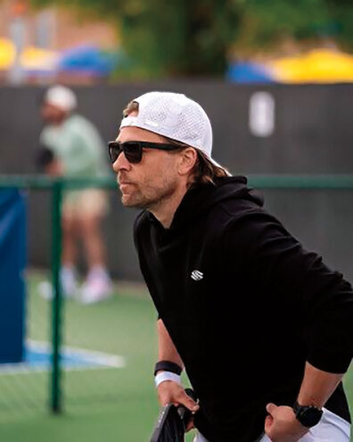 Profile of middle-aged man in sunglasses, black hoodie, and white baseball cap focusing intensely