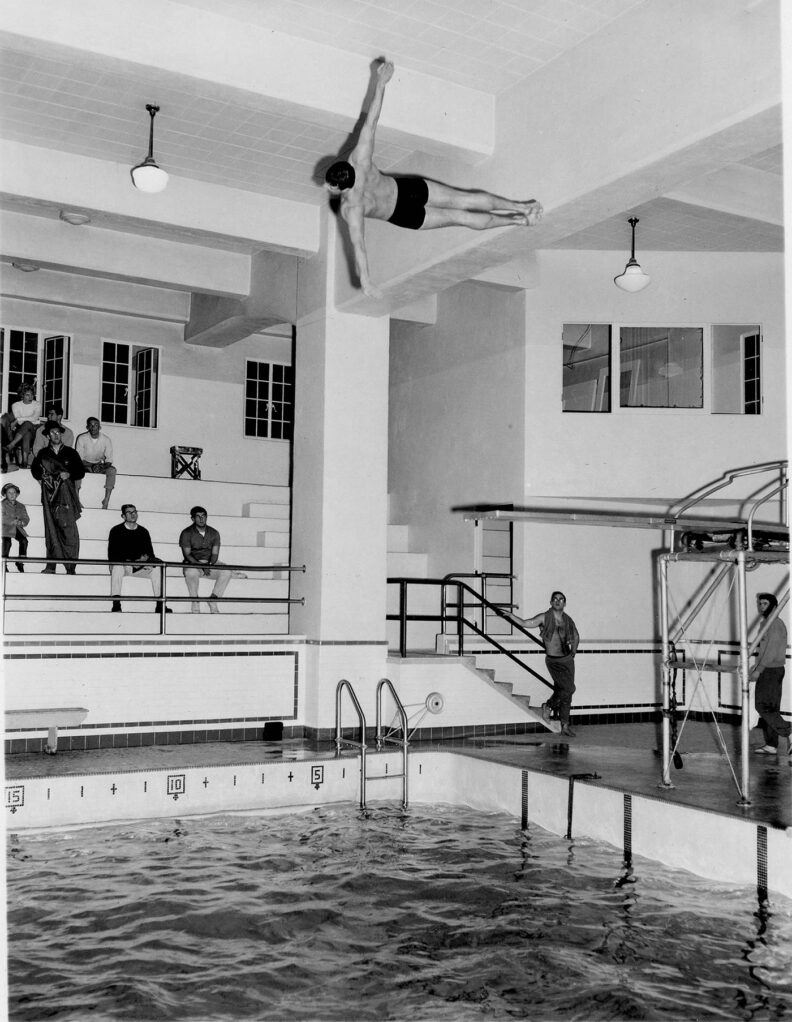 Black and white photo of a young man mid-dive off the high diving board