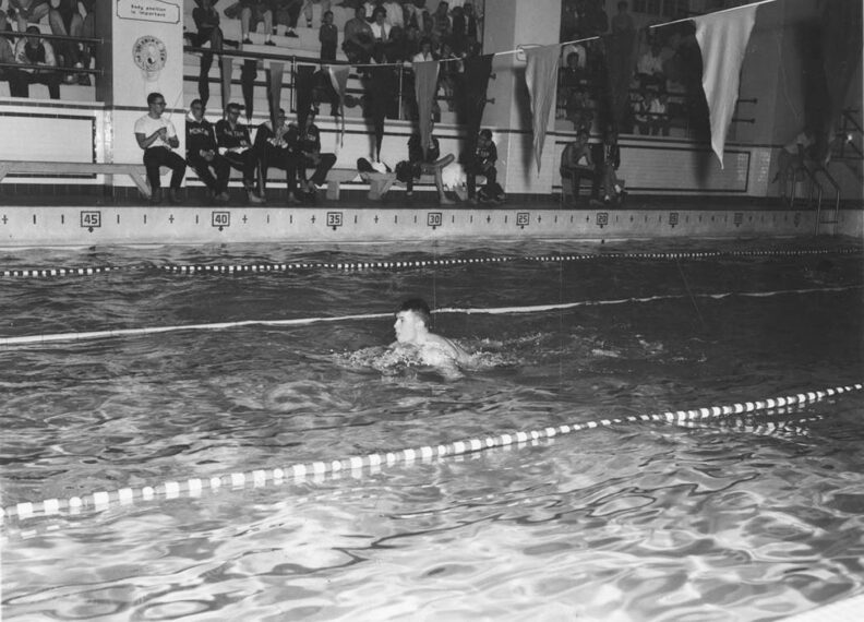 black and white photo of young male swimmer in a race in a pool with lanes