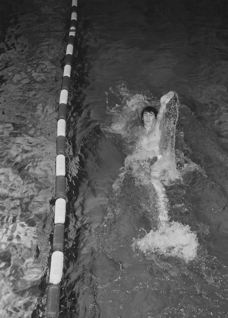 black and white photo of a young man swimming backstroke along a racing lane
