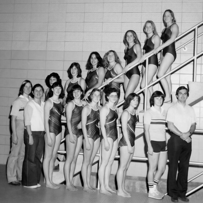Group of young women swimmers standing on stairs with male coach to the side