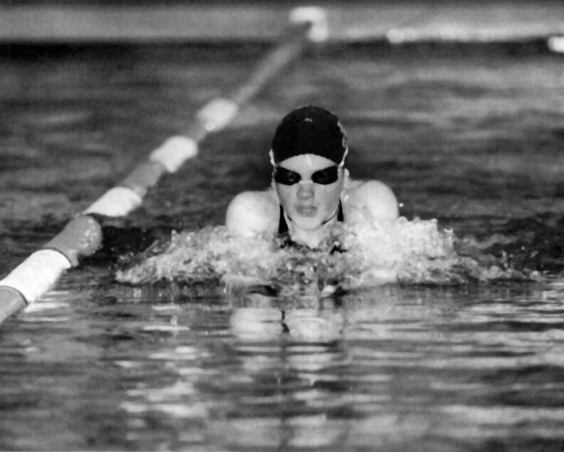 Young woman swims in goggles and swim cap along a racing lane