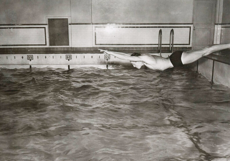 Black and white photo of a young man diving into a pool to practice a swim race