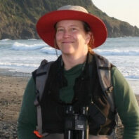 Woman on a beach in a hat and coat with binoculars