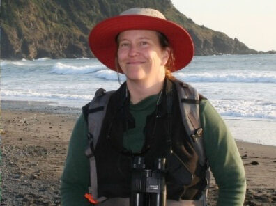 Woman on a beach in a hat and coat with binoculars