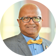 Headshot of Dipra Jha wearing glasses in blazer and bow tie