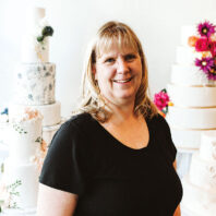 Megan (Peck) Leifson stands in front of several elegant cakes