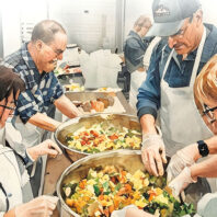 Group of people prepare vegetables in large bowls