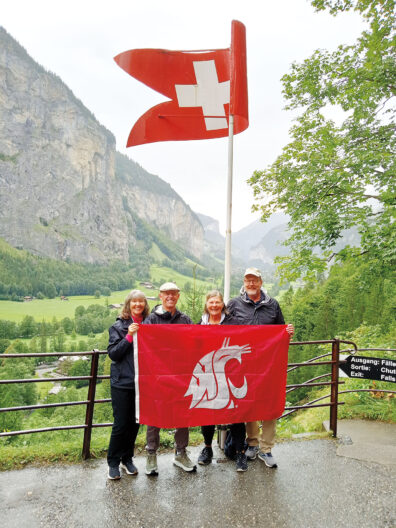 Four people holding a WSU flag in the foreground, with Switzerland flag above and mountain and waterfall background