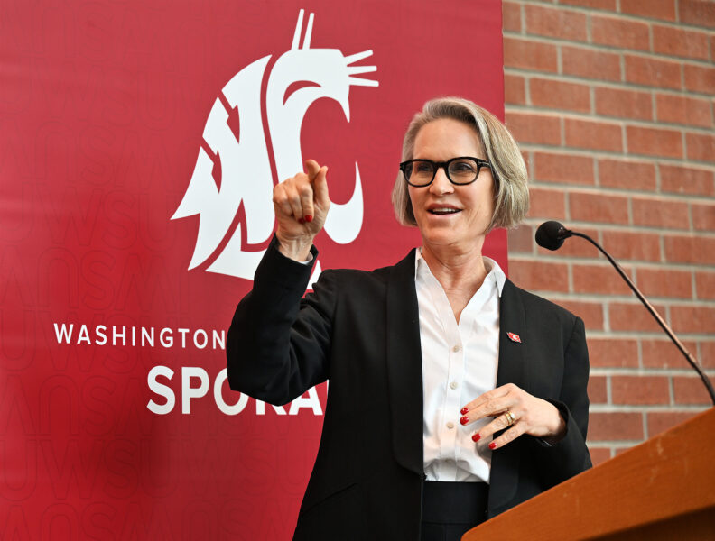 Washington State University President Betsy Cantwell speaks at a lectern in front of a WSU Spokane sign.