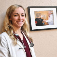 Dr. Christie Kirkpatrick Schmutz in white doctor's coat in front of a wall