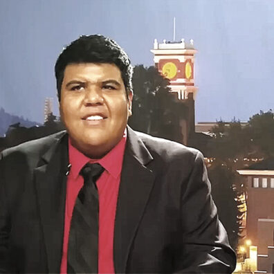 Freddy Llanos in black suit coat and tie with red shirt in front of WSU background