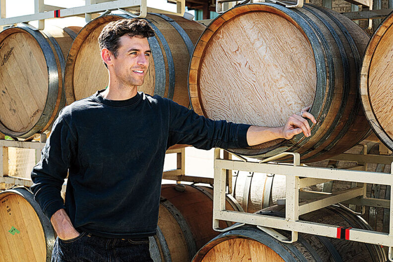 Kenny McMahon stands in front of wine barrels