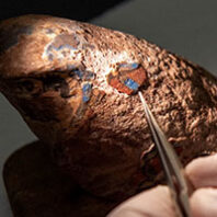 Closeup of ancient wood falcon decoration with a metal instrument removing paint chip
