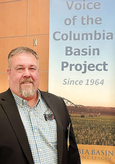 Craig Simpson stands in front of a poster that reads Voice of the Columbia Basin Project Since 1964