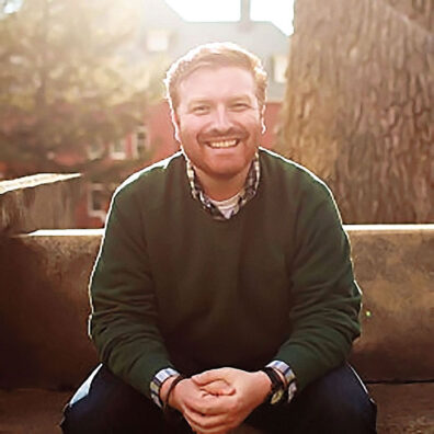 Kevin Schilling sitting on a bench outside, wearing a green sweater