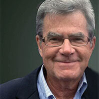Small cropped thumbnail of a close-up photograph showing an older adult wearing glasses and a collared shirt against a dark background.