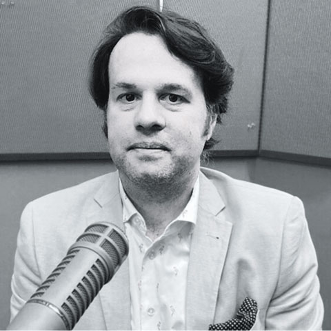 Black-and-white photo of a man seated at a microphone in a recording studio