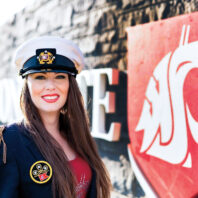 Woman in uniform standing near a wall-mounted Cougar logo sign outdoors.