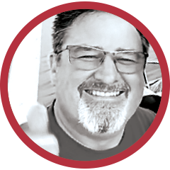 Circular black-and-white portrait of a smiling man wearing glasses, framed by a red border