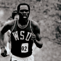 Black‑and‑white photo of a runner wearing a WSU uniform, mid‑stride on a track