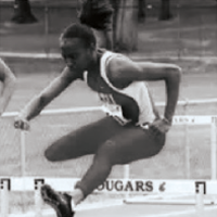 Black‑and‑white photo of a runner wearing a WSU uniform, jumping hurdles on a track