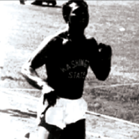 Black‑and‑white photo of a runner wearing a WSU uniform, mid‑stride on a track