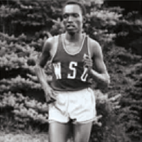Black‑and‑white photo of a runner wearing a WSU uniform, mid‑stride with trees in background