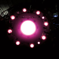 View into a fusion research device showing a bright circular core surrounded by evenly spaced glowing lights inside a dark chamber.