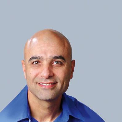 Head-and-shoulders studio portrait of a man with a shaved head wearing a blue collared shirt against a light gray background.