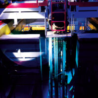 Overhead view of an industrial research facility with platforms and railings surrounding a deep, illuminated chamber reflecting blue light.