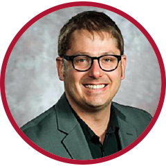 Circular headshot of a man wearing glasses and a dark jacket, framed by a red border against a studio-style background.