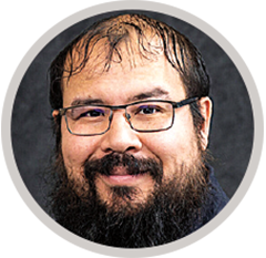 Circular headshot of a man with a beard, framed by a light gray border against a dark background.