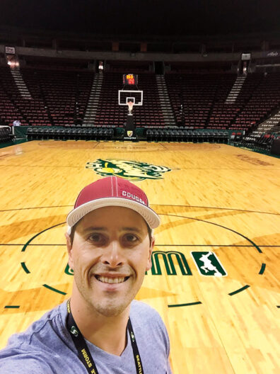 Young man in a WSU Cougars baseball cap takes a selfie on court of the Seattle Storm basketball team.