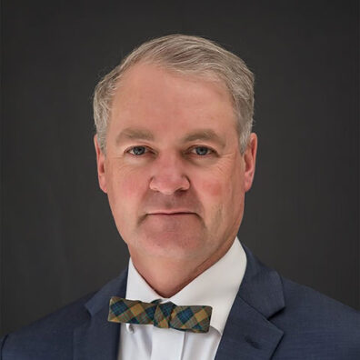 Studio portrait of a man wearing a suit jacket and patterned bow tie against a dark background.