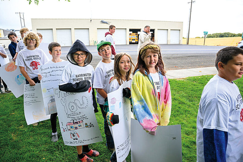 Line of schoolchildren standing outdoors on grass, holding signs near a school building.