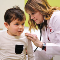 Healthcare provider uses a stethoscope to examine a young child during a medical appointment in an exam room.