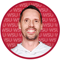 Head-and-shoulders portrait of a person wearing a light gray hoodie against a crimson background patterned with repeated “WSU” text.