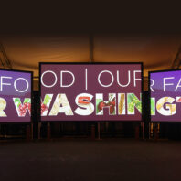 Three large digital screens display the message “Our Food, Our Farms, Our Washington,” with letters filled with illustrations of agricultural products and crops at an indoor exhibition.