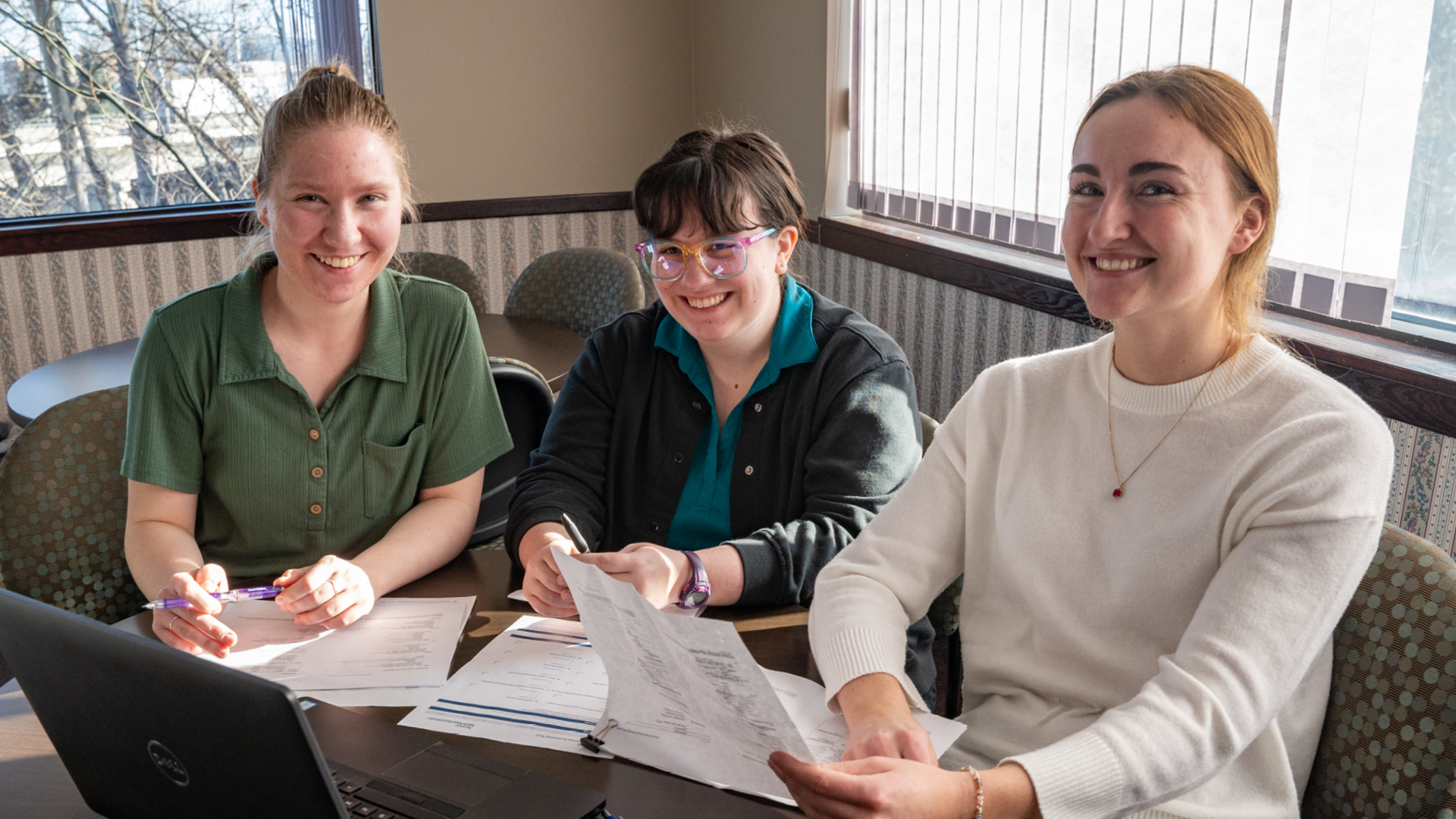 Students smiling at a table working on a laptop