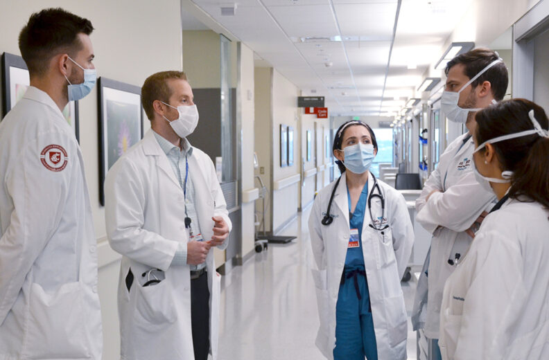 Groups of residents talking to program director in the hallway of a hospital.