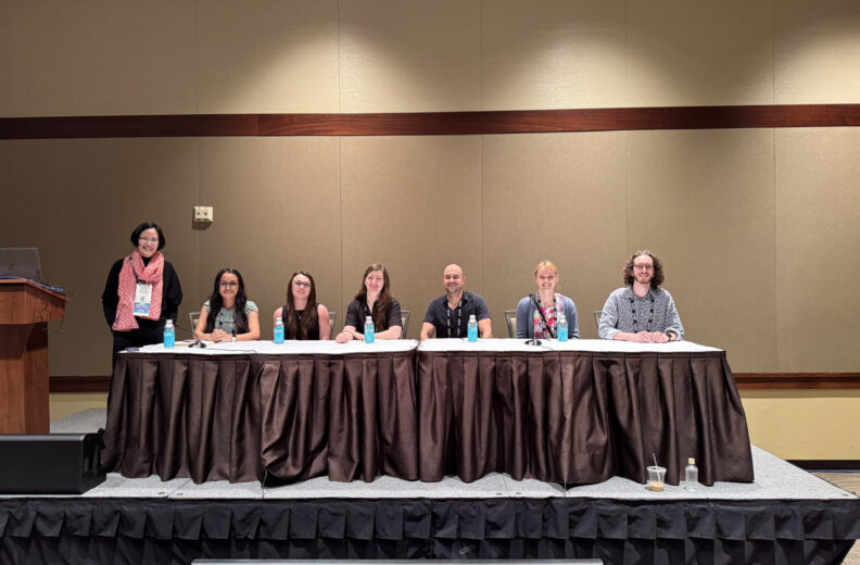 Seven people sitting at a long table at a conference.