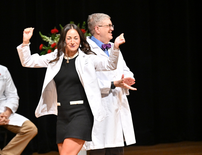 Happy MD student walking across stage after getting their white coat.