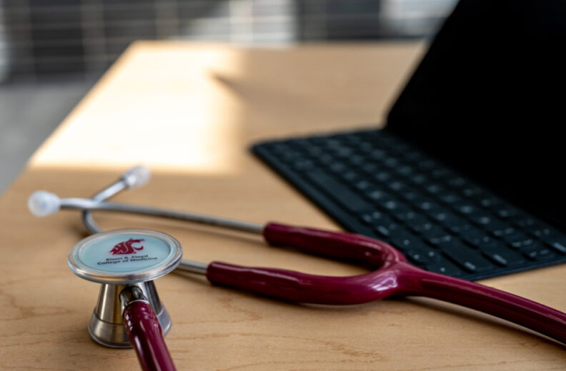Laptop and a stethoscope that has a WSU logo, sitting on a desk.