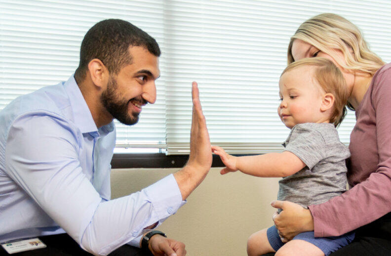 A doctor reaching out for a high five to a mother and toddler.