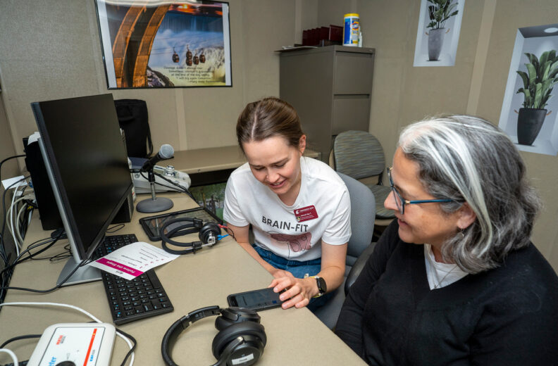 Two people sitting at a desk in an office looking at a phone together.