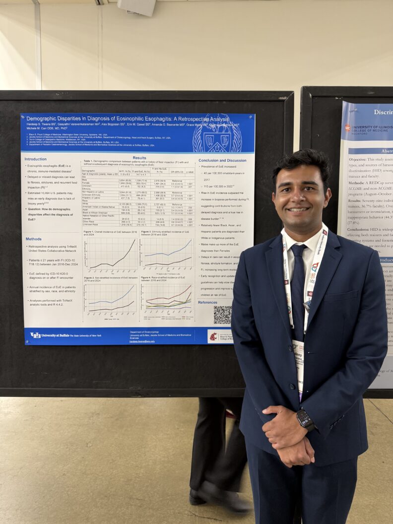 A person wearing a dark suit and tie stands in front of a large academic poster displayed on a black board. The poster has a blue header and contains multiple sections of text, tables, and line graphs. The header includes a university logo and title, and the bottom section features institutional affiliations. Another poster is partially visible to the right, and the setting appears to be an indoor conference or academic event.