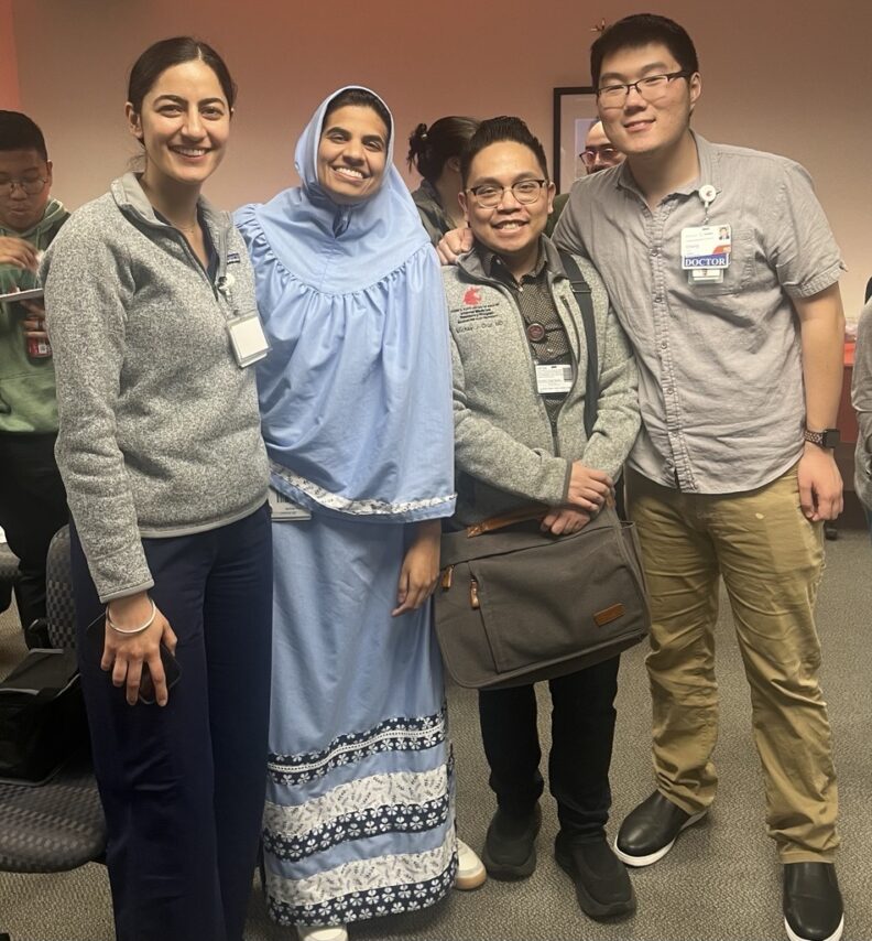 A group of 4 people standing side by side, smiling. 